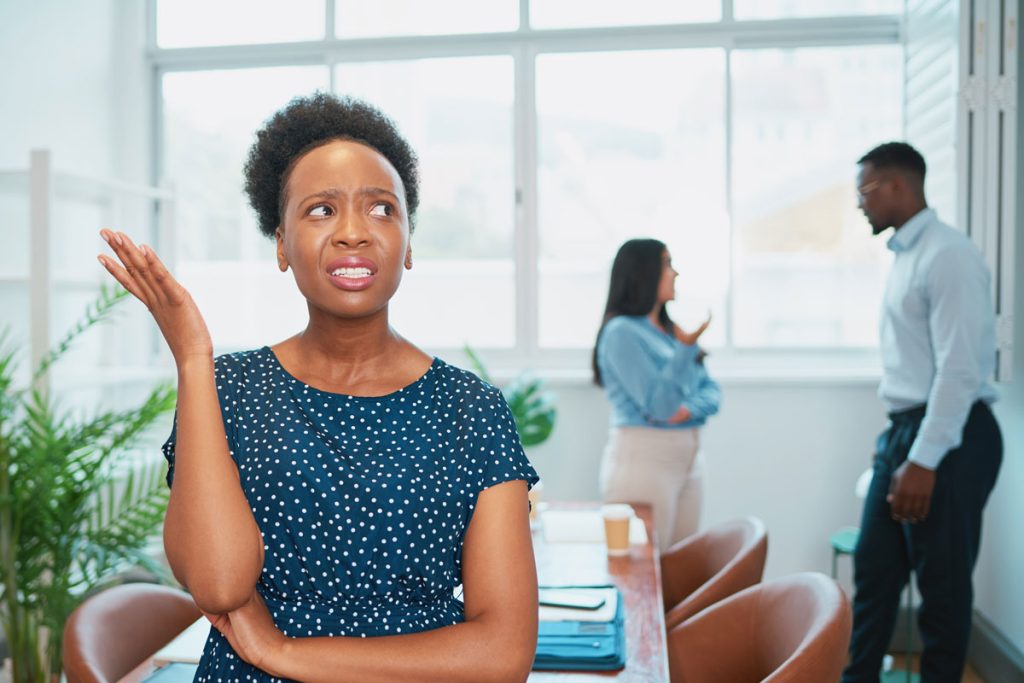 Young Black Woman Looks Upset While Colleagues Talk Behind Her Back Office Drama Young Black Woman Looks Upset While Colleagues Talk Behind Her Back Office Drama